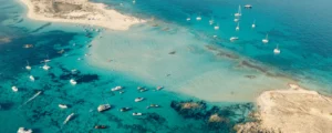 Aerial view of yachts, catamarans and motorboats anchored in turquoise shallows between two sandy points