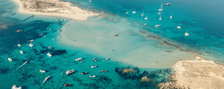 Aerial view of yachts, catamarans and motorboats anchored in turquoise shallows between two sandy points