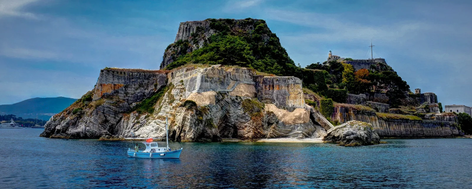 The Old Fortress of Corfu Town seen from the sea, with a small boat at anchor below its cliffs