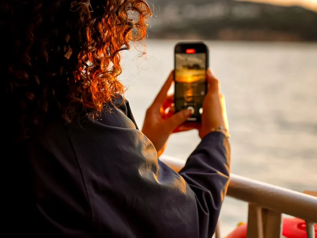 A passenger photographing the sunset from the deck of a ferry