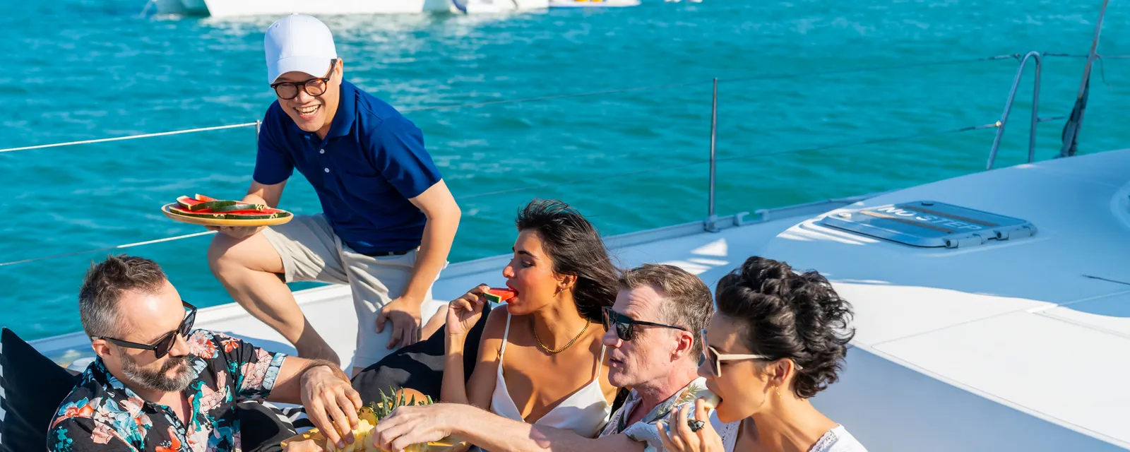 Friends sharing fruit on the deck of a charter catamaran with their skipper