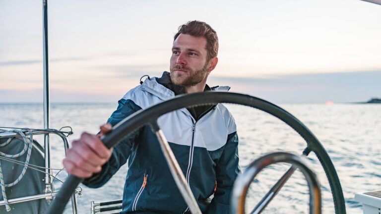 Skipper at the helm of a sailing yacht at sunset