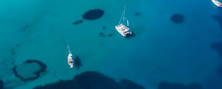 Sailing catamaran and yachts anchored in clear turquoise water, seen from above