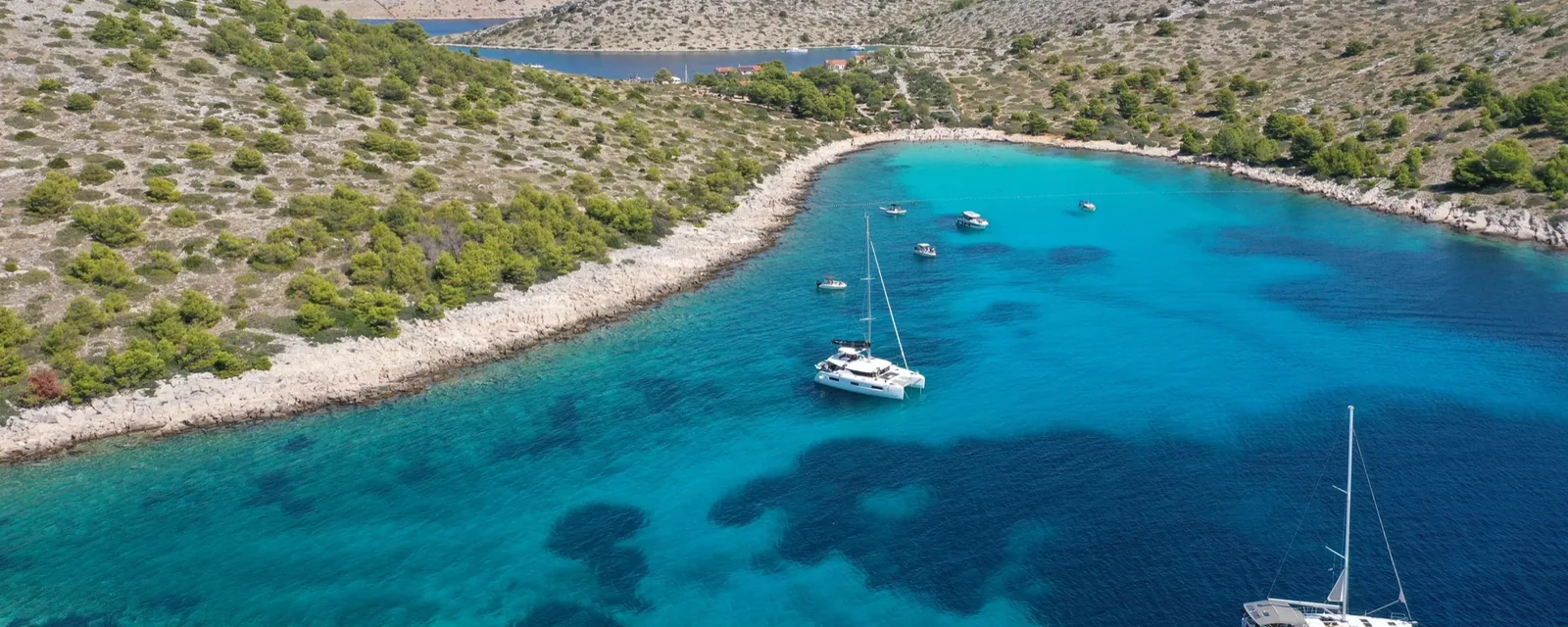 Aerial view of two sailing yachts anchored in a turquoise cove between low rocky islands