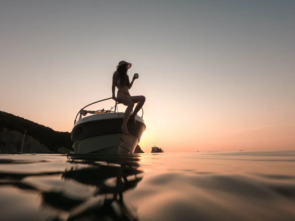 A woman sitting on the bow of a small motorboat at anchor at sunset