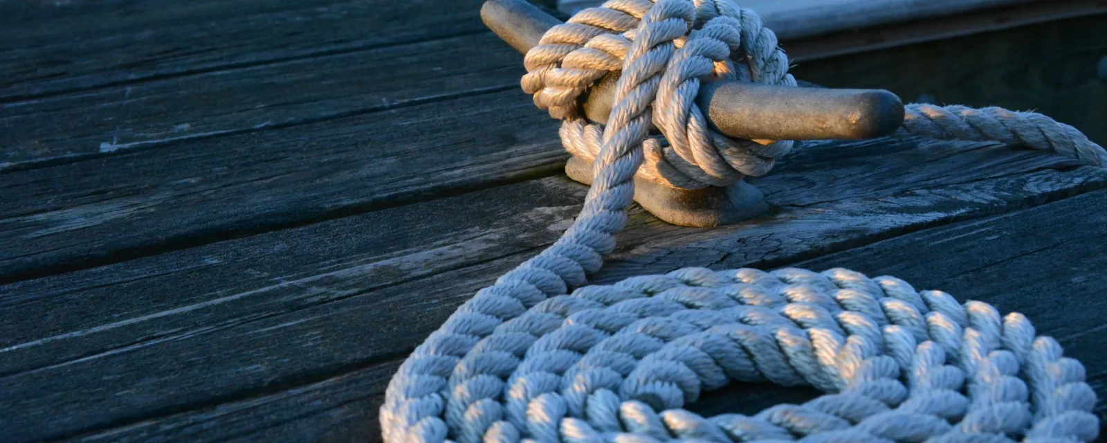 Mooring rope coiled and tied to a cleat on a wooden dock at golden hour