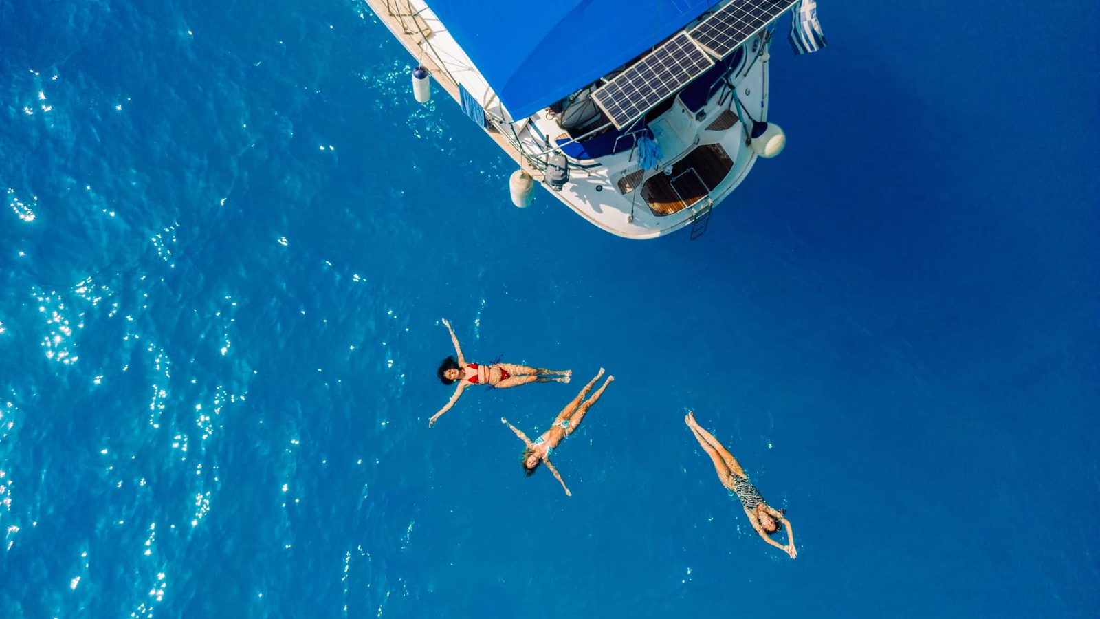 Swimmers floating beside a sailing yacht in clear blue Greek waters in summer