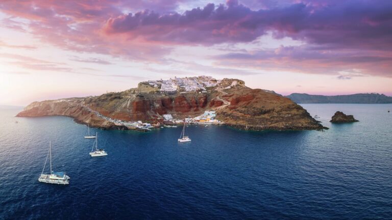Sailing yachts and catamarans anchored below Oia and Ammoudi Bay, Santorini, at sunset